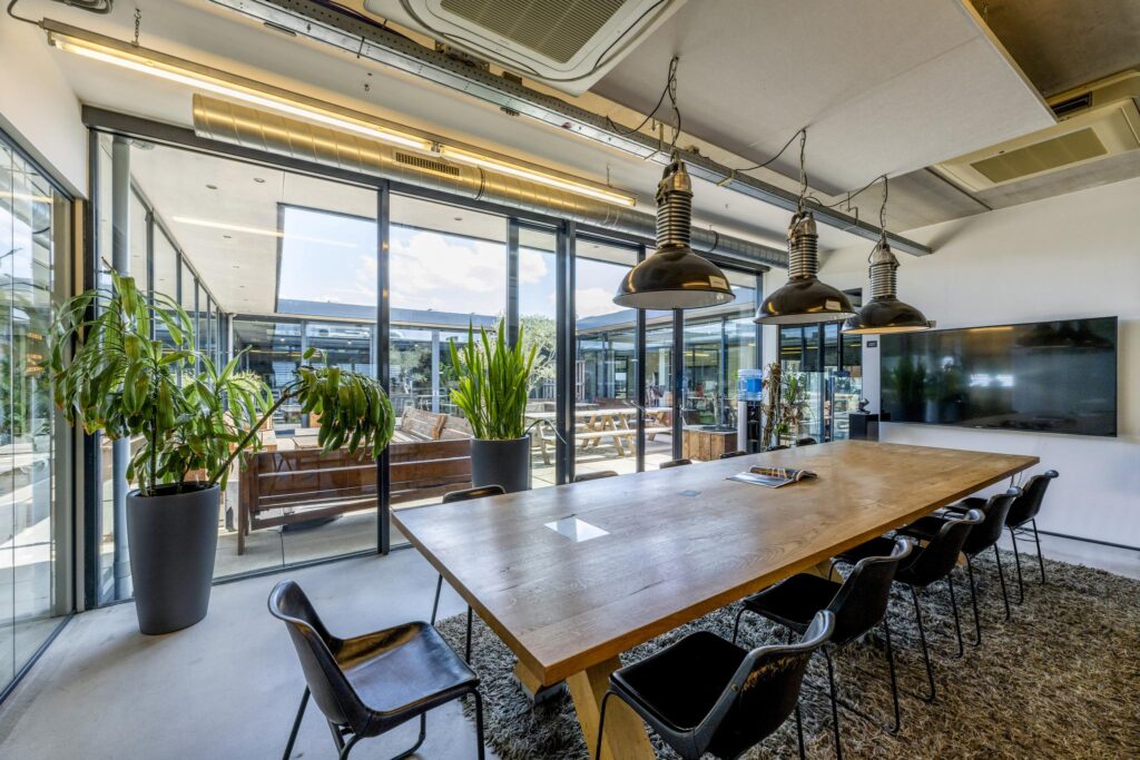 Modern meeting room on Johan van Hasseltweg with a large wooden table, black chairs, and glass walls overlooking an outdoor seating area.